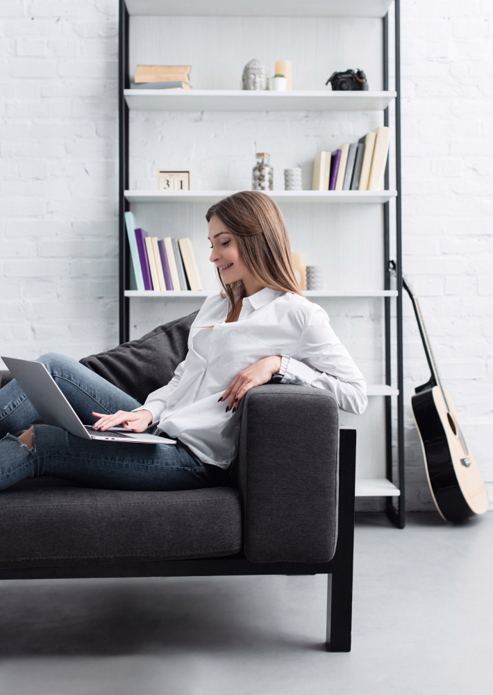 Mujer sentada en un sofa escribiendo en un portátil