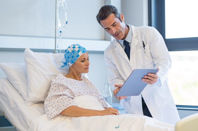 Mujer joven con cáncer en la cama de un hospital hablando con su médico