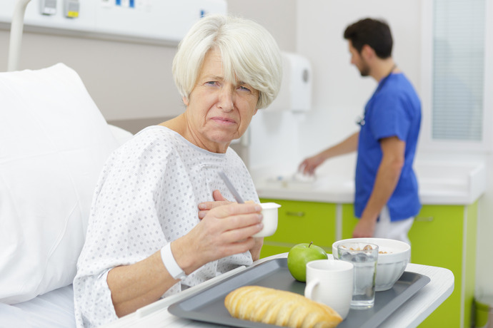 Mujer comiendo en cama de hospital con gesto de malestar